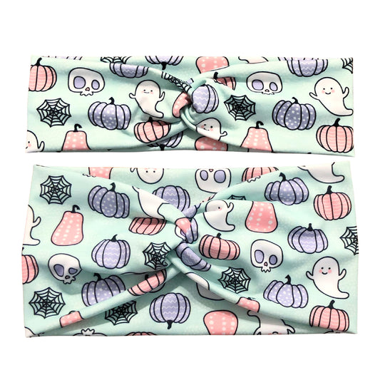 Fabric headband with Halloween-themed pattern featuring pumpkins, ghosts, and spiders on a light blue background.